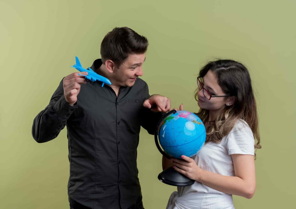 Two people standing facing each other and holding a miniature plane world globe in their hands.